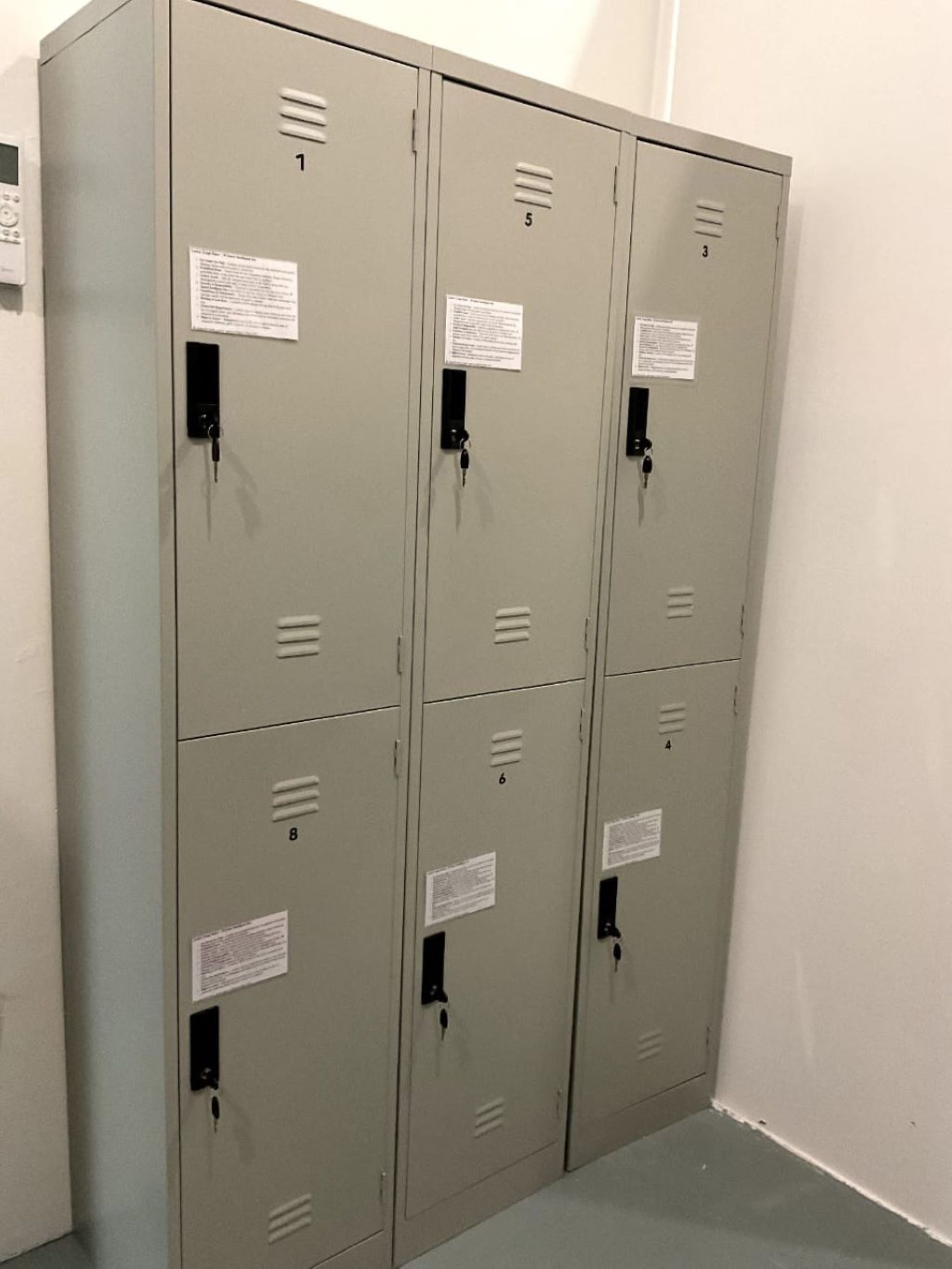 A row of grey metal lockers with numbered compartments, each with a keyhole and a small label.