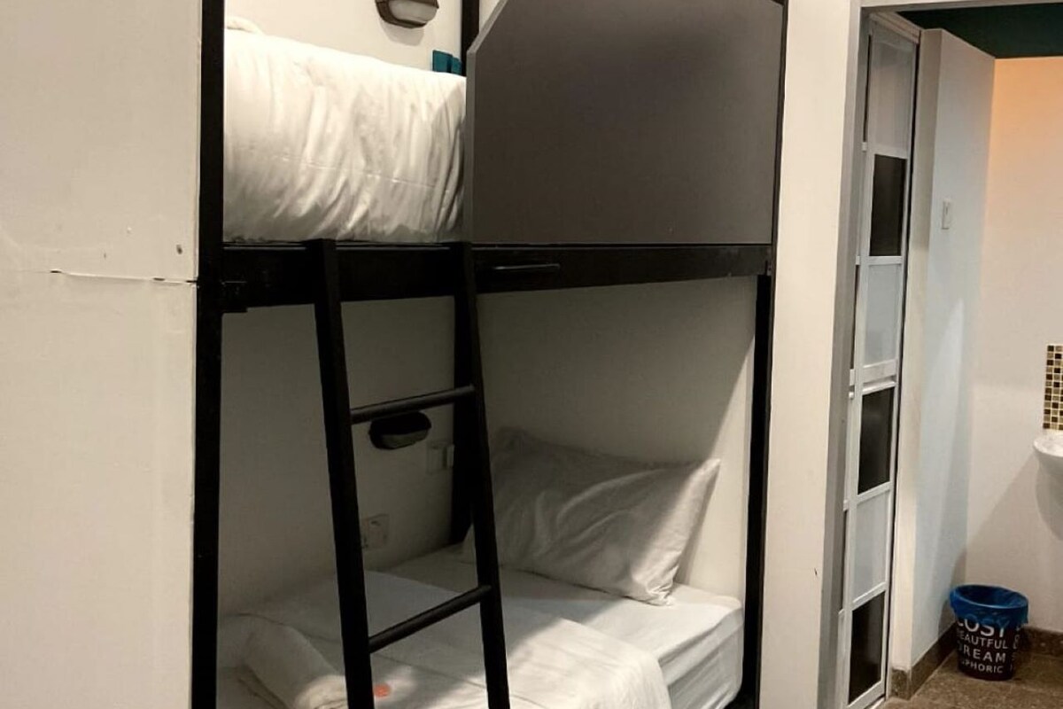 Een slaapkamer met stapelbed, een ladder, een klein plankje en een deur naar een andere kamer.