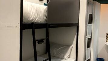 Habitación con literas, una escaleta, un pequeño estante y una puerta que da a otra habitación.