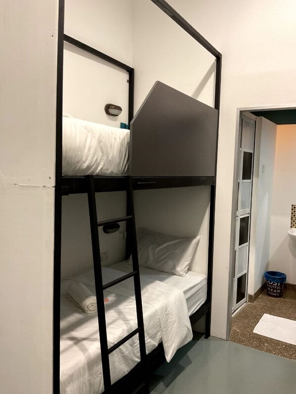 Ein Schlafzimmer mit Etagenbetten, einer kleinen Ablage und einer Tür zu einem weiteren Raum.
