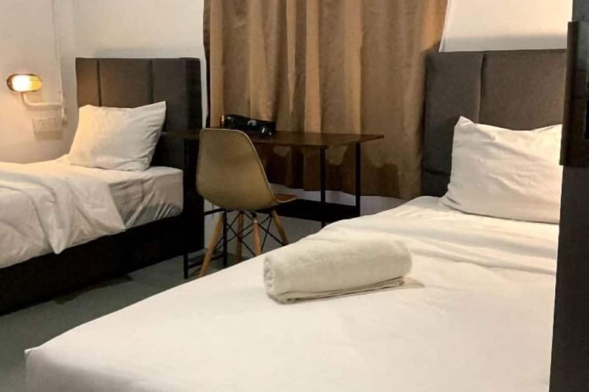 A hotel room with two beds, a small table, a chair, and a lamp.