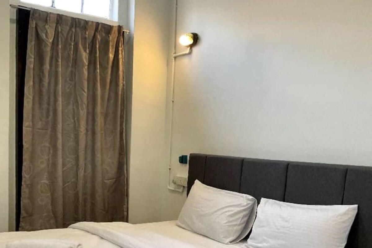 A neatly made bed with white linens and pillows, a dark headboard, and a window with curtains.