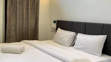 A neatly made bed with white linens and pillows, a dark headboard, and a window with curtains.