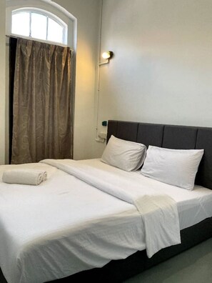 Cama bem arrumada com lençóis e almofadas brancos, uma cabeceira escura e uma janela com cortinas.
