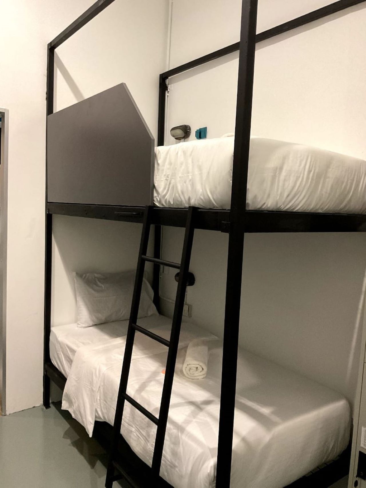 A bunk bed with a ladder, white bedding, and a small shelf with a lamp and a book.