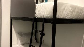 A bunk bed with a ladder, white bedding, and a small shelf with a lamp and a book.