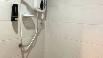 A shower area with a handheld showerhead, a wall-mounted control panel, and a soap dispenser.