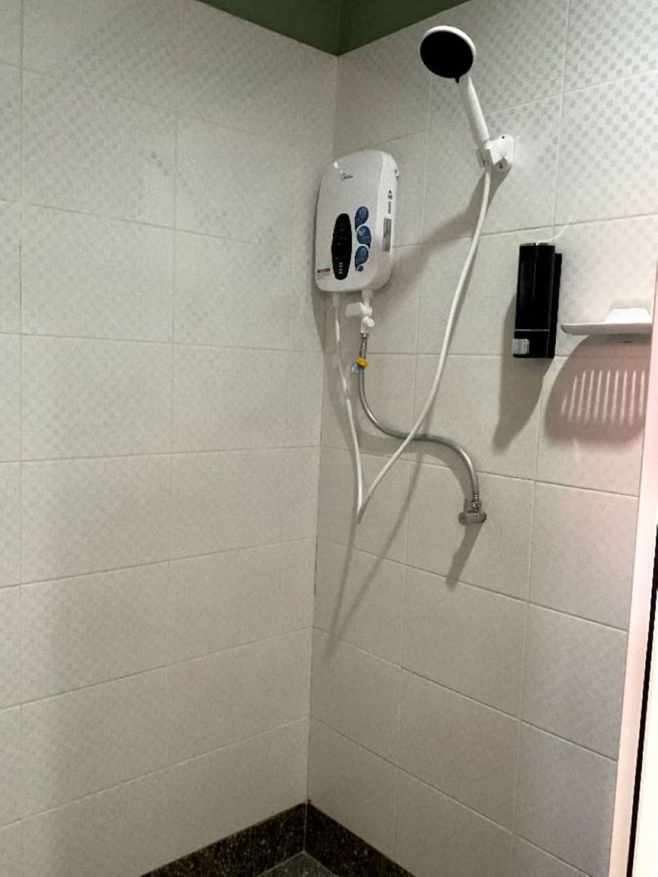 A shower area with a handheld showerhead, a wall-mounted control panel, and a handheld soap dispenser.