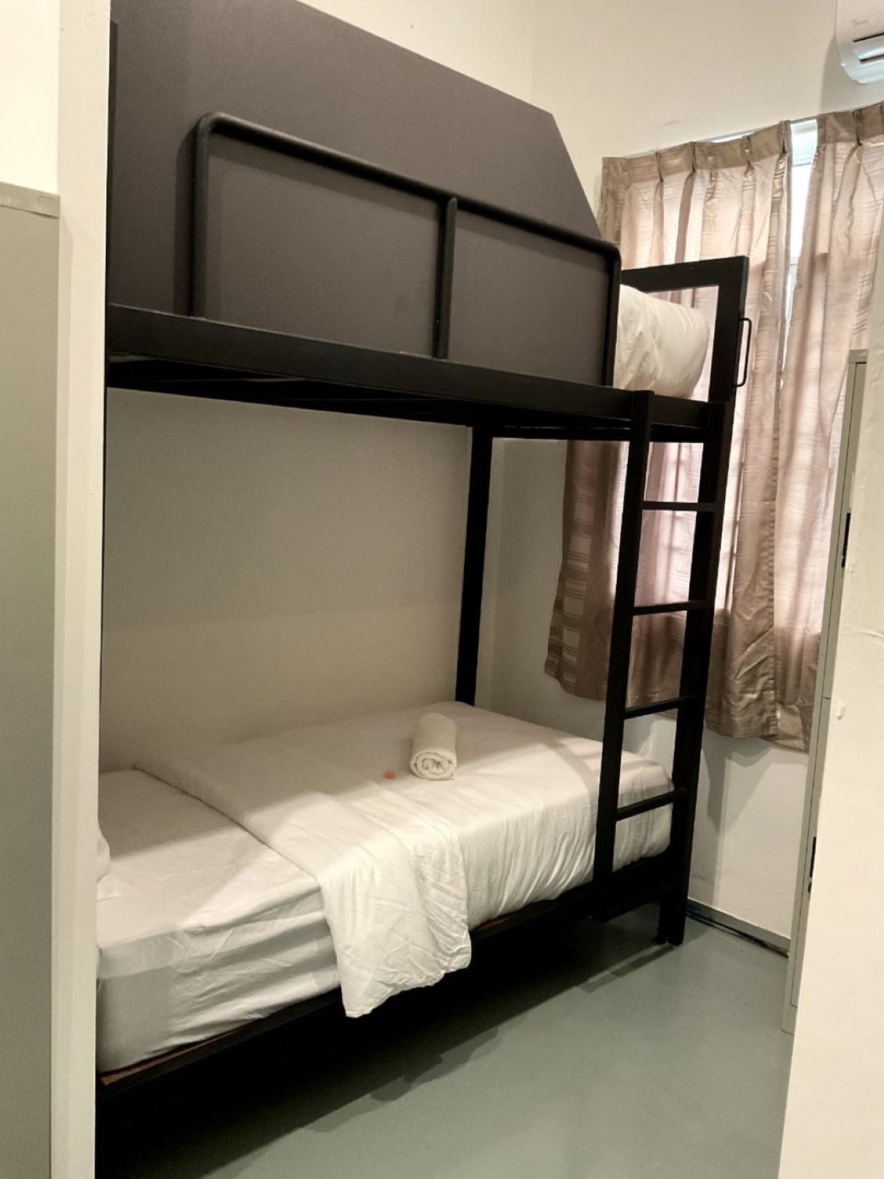 A bunk bed with a ladder, a white mattress, and a rolled-up towel.