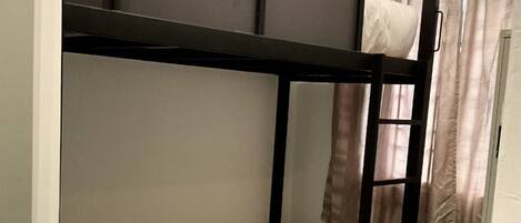 A bunk bed with a ladder, a white mattress, and a rolled-up towel.