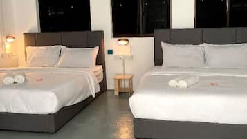 A hotel room with two beds, each with white bedding and pillows, a small wooden nightstand, and a wall-mounted lamp.