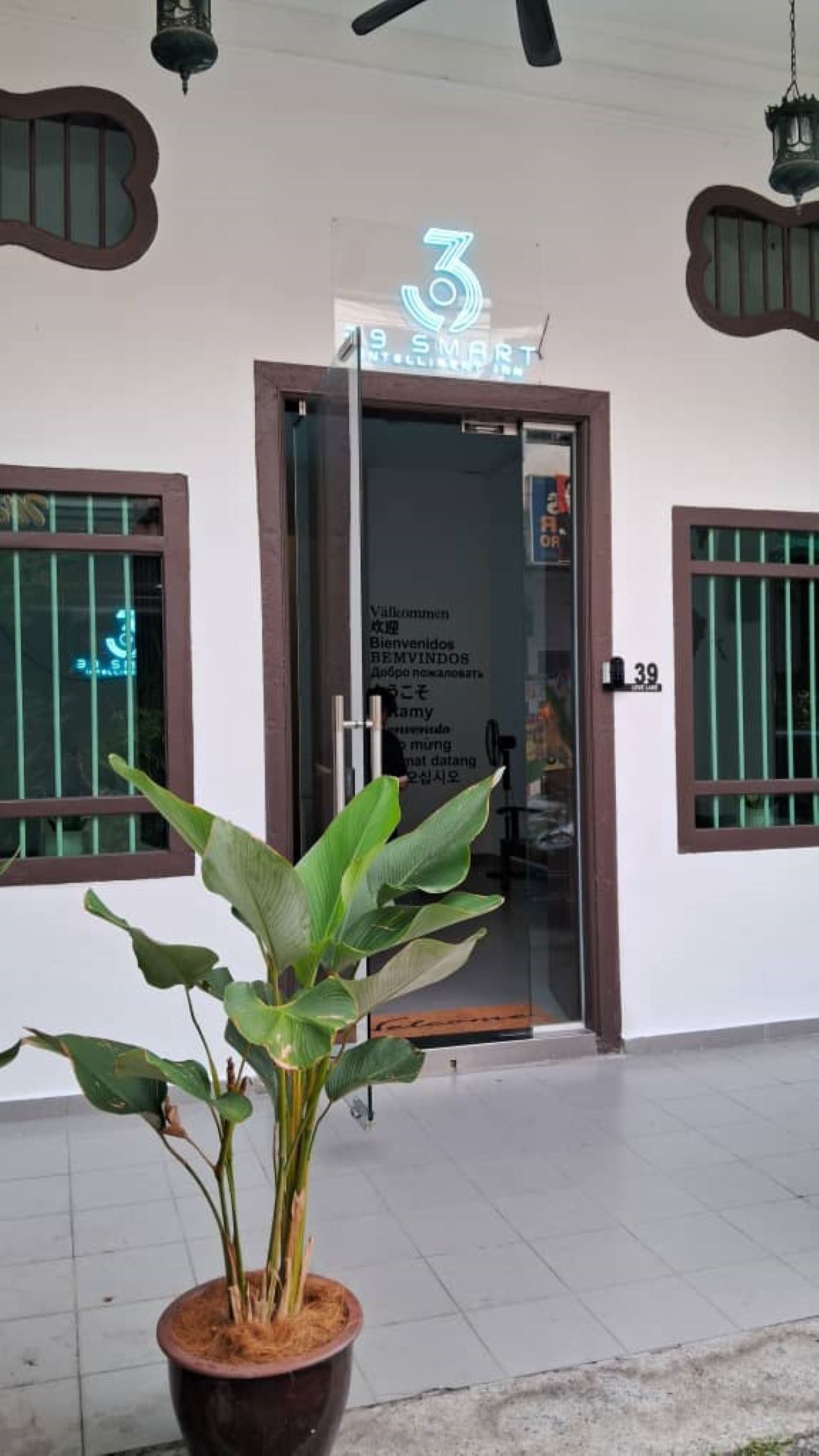 Entrada de hotel con letrero de neón, una planta en maceta y una puerta con número.