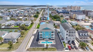 Una zona residencial costera con un edificio azul destacado que tiene una piscina, rodeado de varias casas y edificios.