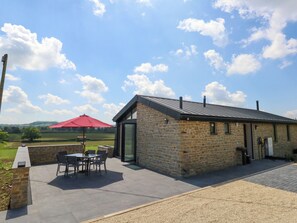 A stone building with a metal roof, a patio with a table and chairs, and a red umbrella. - Frogwell (Sherborne)