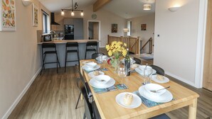 Zona pranzo con tavolo di legno apparecchiata per quattro, cucina sullo sfondo e una scala che conduce a un altro piano.