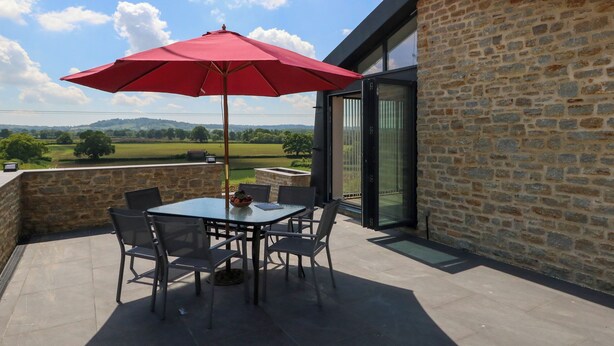 Un patio con tavolo e sedie, un ombrello rosso e vista sulla campagna.