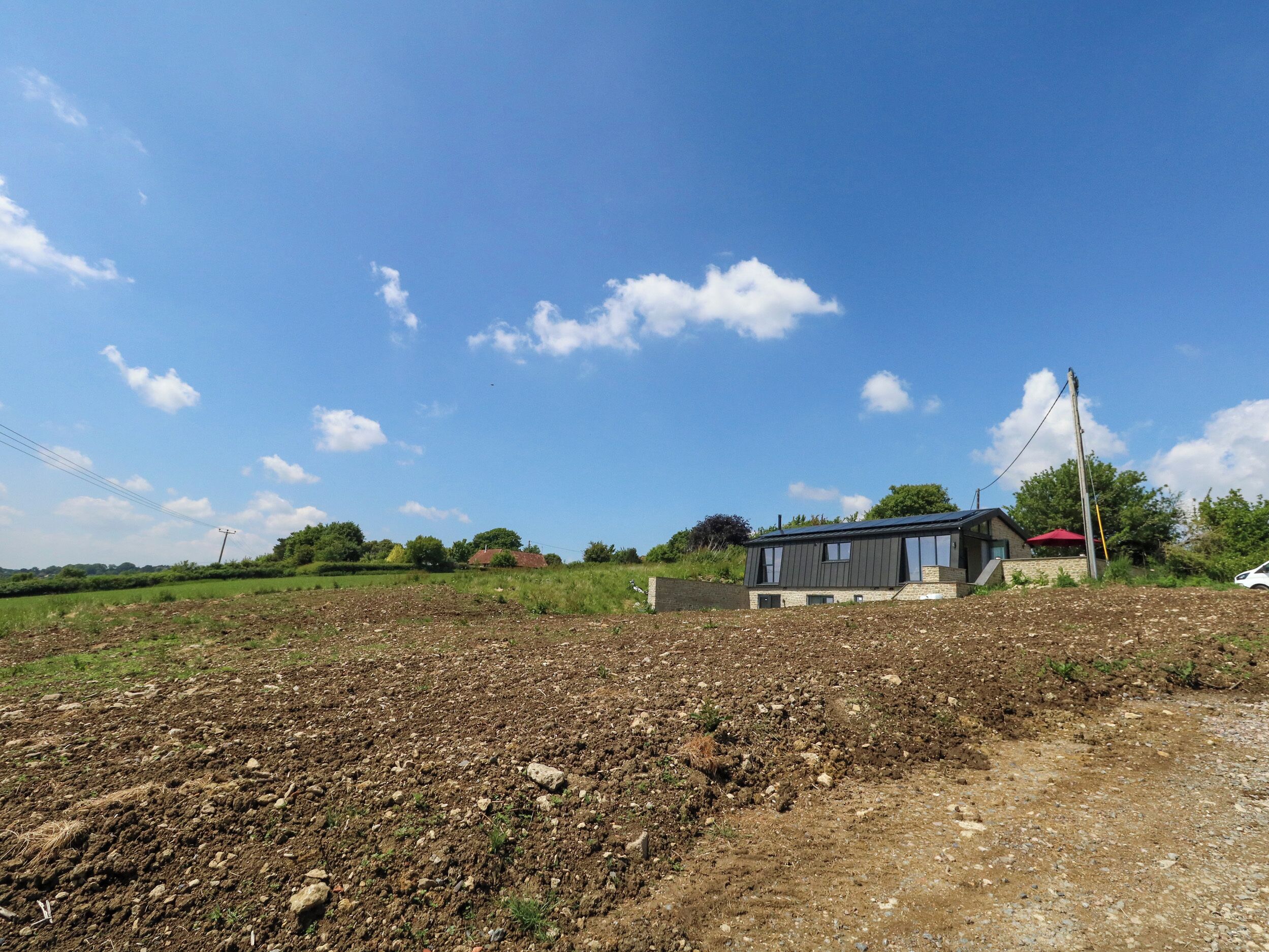 A modern house with a flat roof and large windows, surrounded by a rural landscape with open fields and scattered trees.