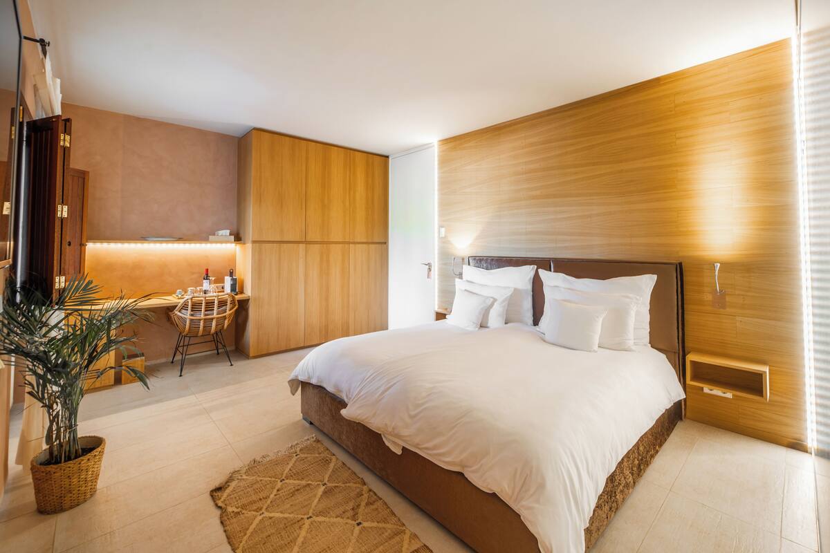 Une chambre moderne avec un grand lit, une tête de lit en bois et un petit espace bureau avec une chaise.