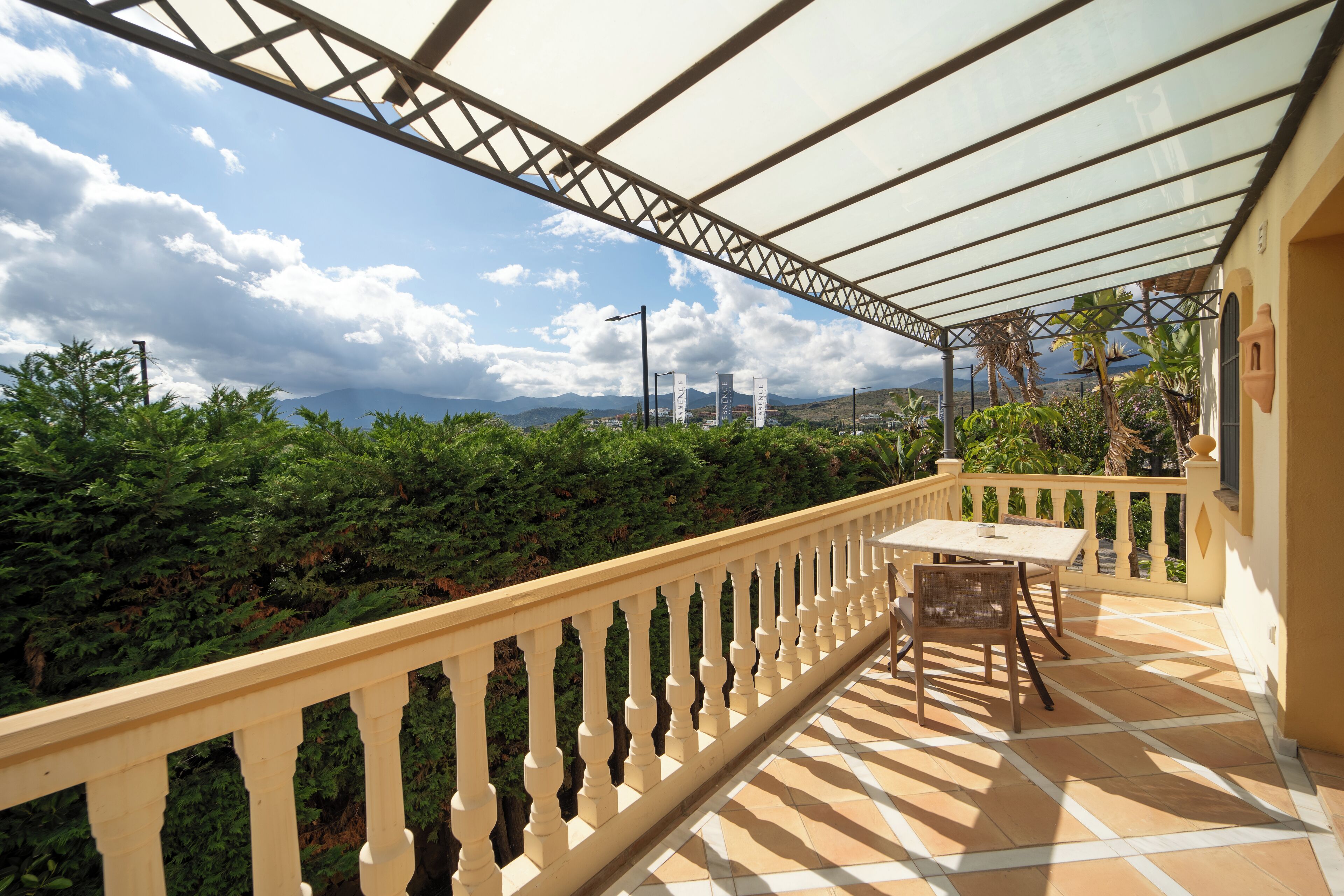 Un balcon offrant une vue sur les montagnes et la verdure, une table et des chaises, ainsi qu’une structure en forme de pergola.
