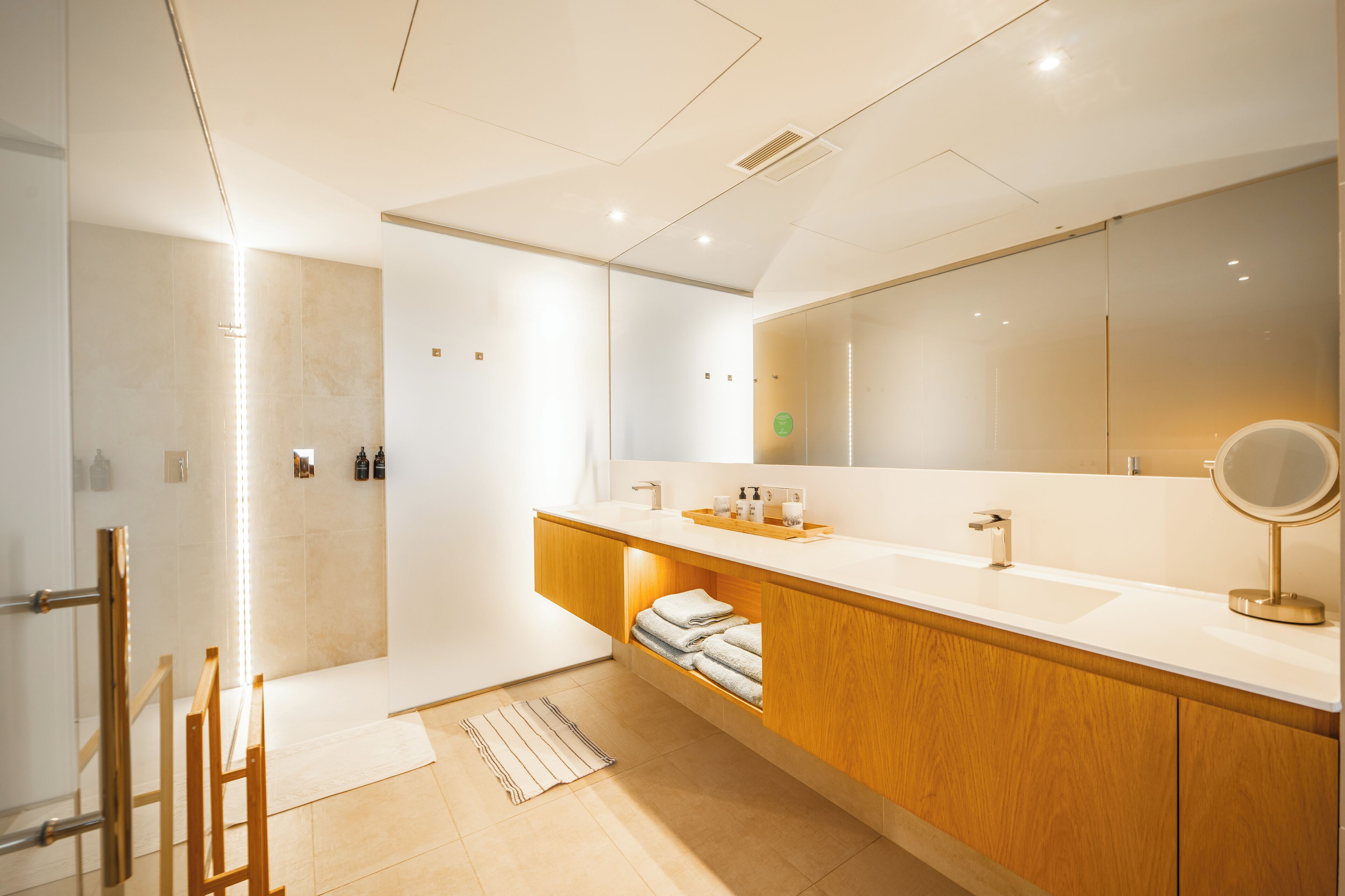 Un baño moderno con un espejo grande, tocador de madera y zona de ducha.