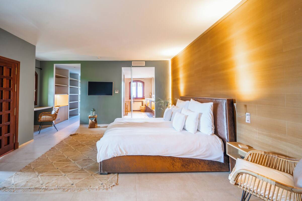 Une chambre spacieuse avec un grand lit, une tête de lit en bois, un téléviseur fixé au mur et une bibliothèque intégrée.