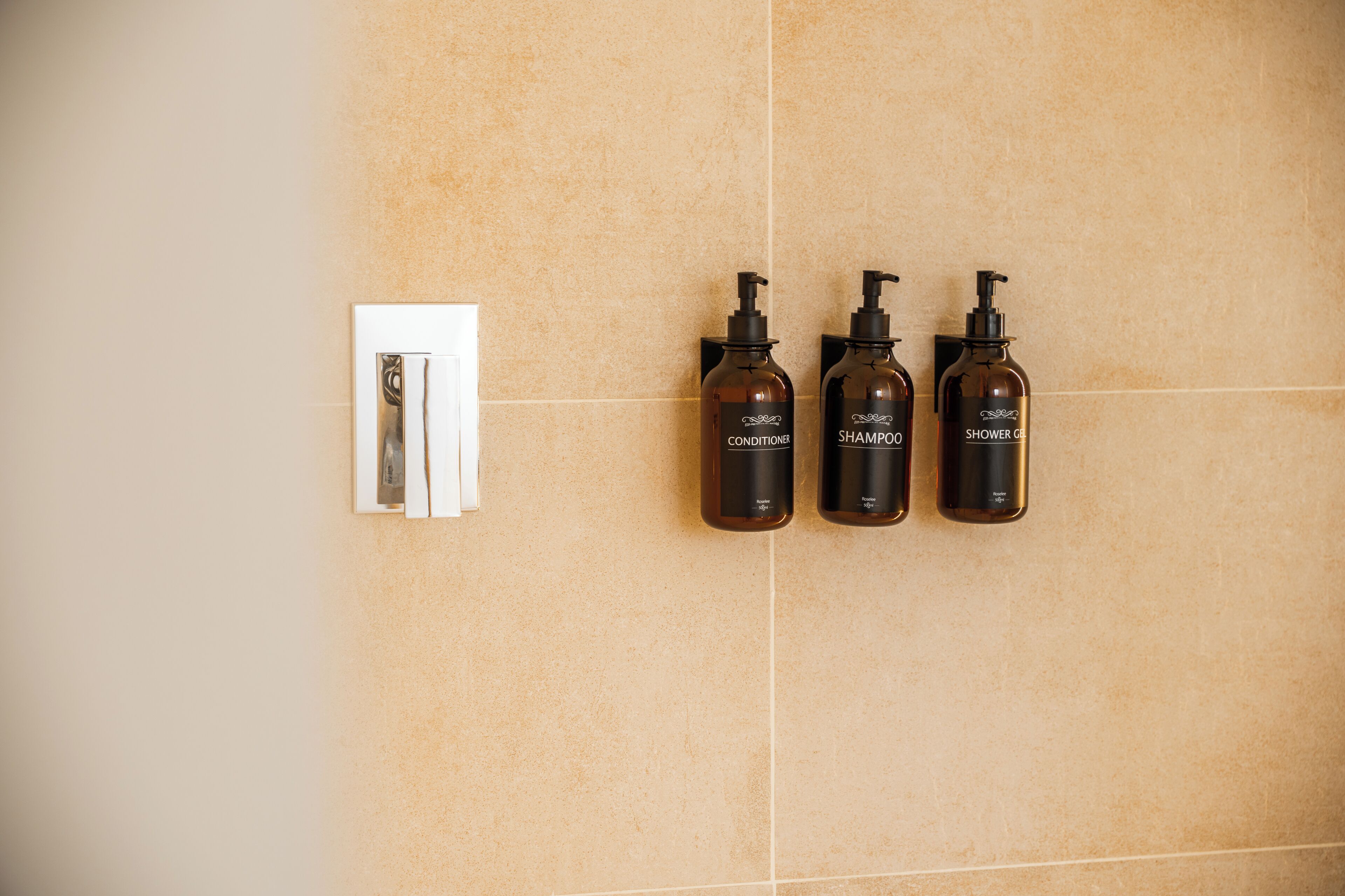 Une salle de bain avec trois bouteilles de shampoing et d’après-shampoing, ainsi qu’un distributeur d’essuie-tout.