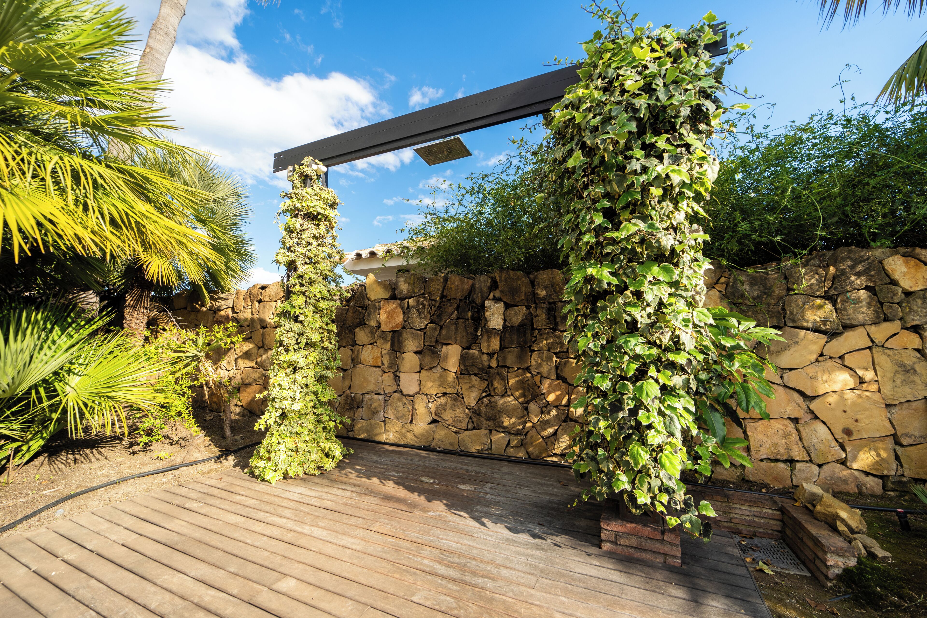 Una terraza de madera con un muro de piedra y una pérgola cubierta de plantas trepadoras.