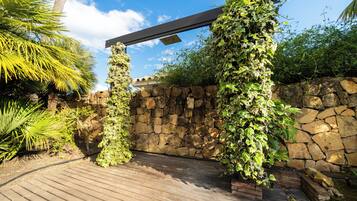 Una terraza de madera con un muro de piedra y una pérgola cubierta de plantas trepadoras.