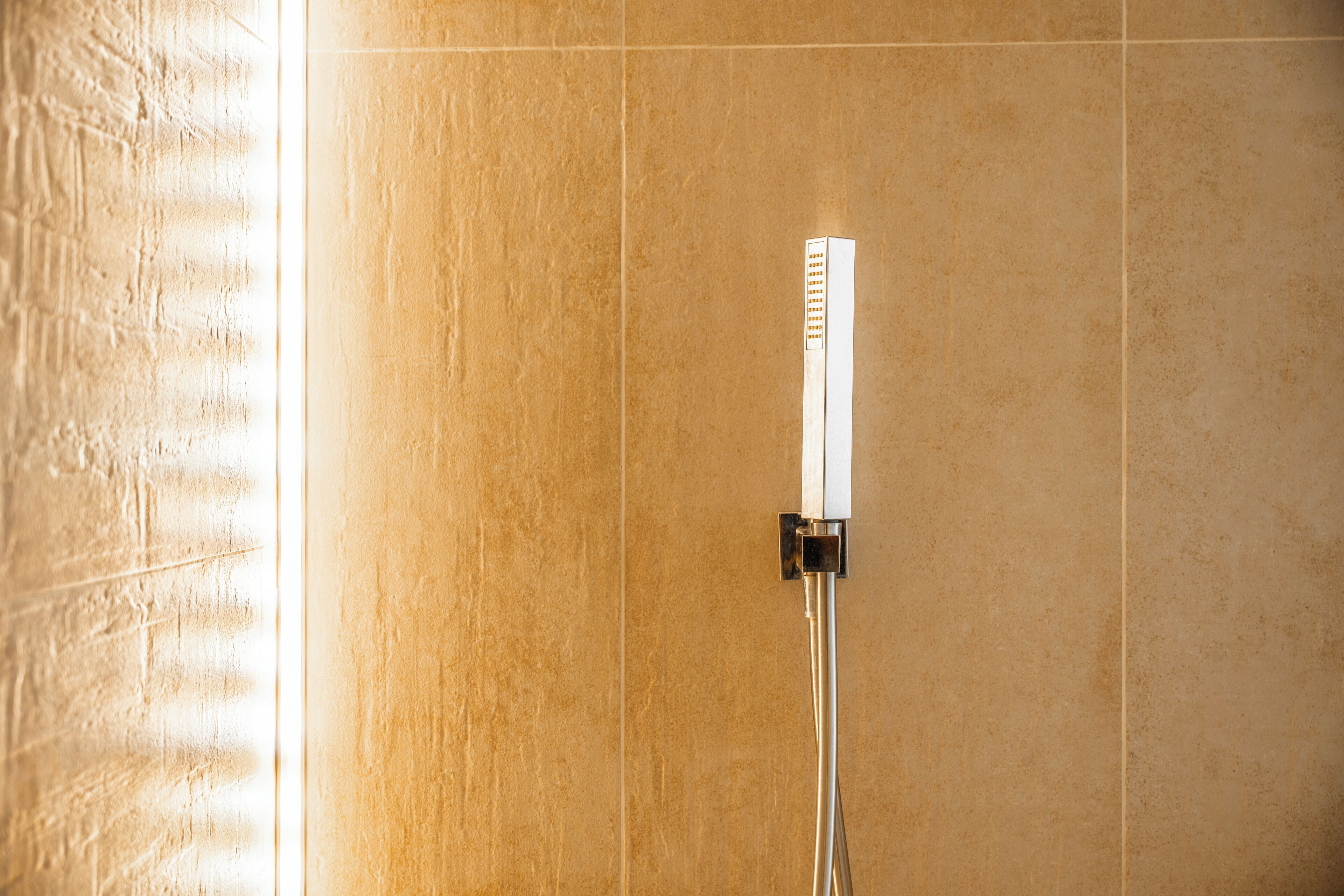 A shower with a chrome hose and wall-mounted controls, set against a tiled wall.