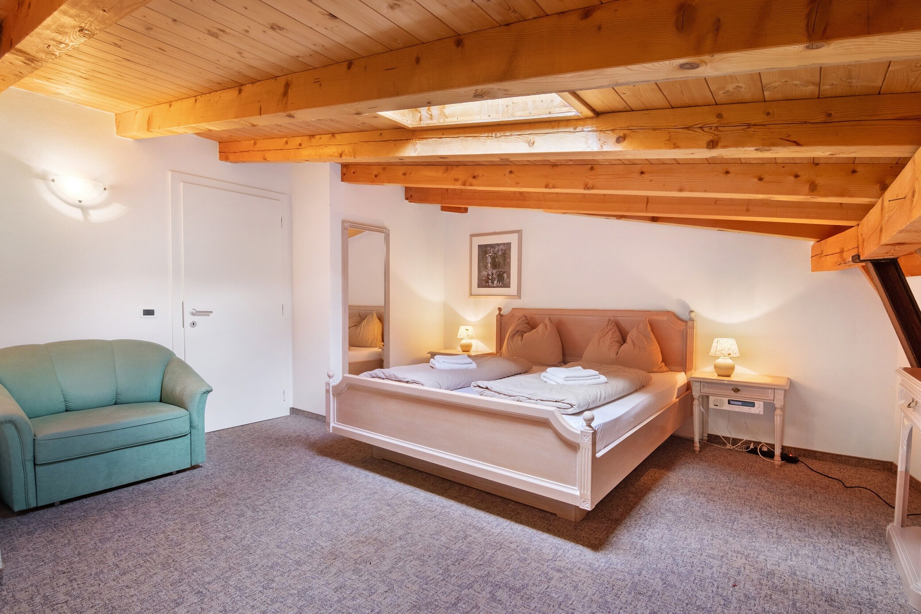 Una camera da letto con un letto, comodini, un divano e un lucernario.