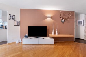 A modern living room with a flat-screen TV on a white stand, a mounted deer skull, and a wall-mounted light. - Apartment 'Am Reschensee' with Mountain View, Balcony and Wi-Fi (San Valentino Alla Muta)