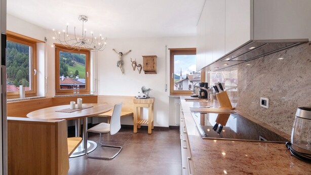 A modern kitchen with a marble countertop, wooden cabinets, and a view of the countryside. - Apartment 'Am Reschensee' with Mountain View, Balcony and Wi-Fi (San Valentino Alla Muta)