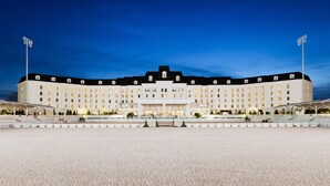 Un hotel grande de varios pisos con una fachada simétrica, una entrada central y un amplio espacio exterior con asientos y una sección cubierta.