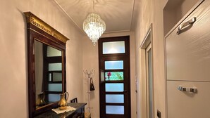Um corredor com uma mesa de madeira escura, um espelho grande, um candelabro e uma porta de vidro fosco.
