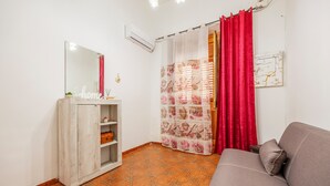 A room with a sofa, a cabinet with shelves, a mirror, a red curtain, and patterned curtains.