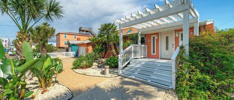 A coastal building with a porch, palm trees, and a clear sky.
