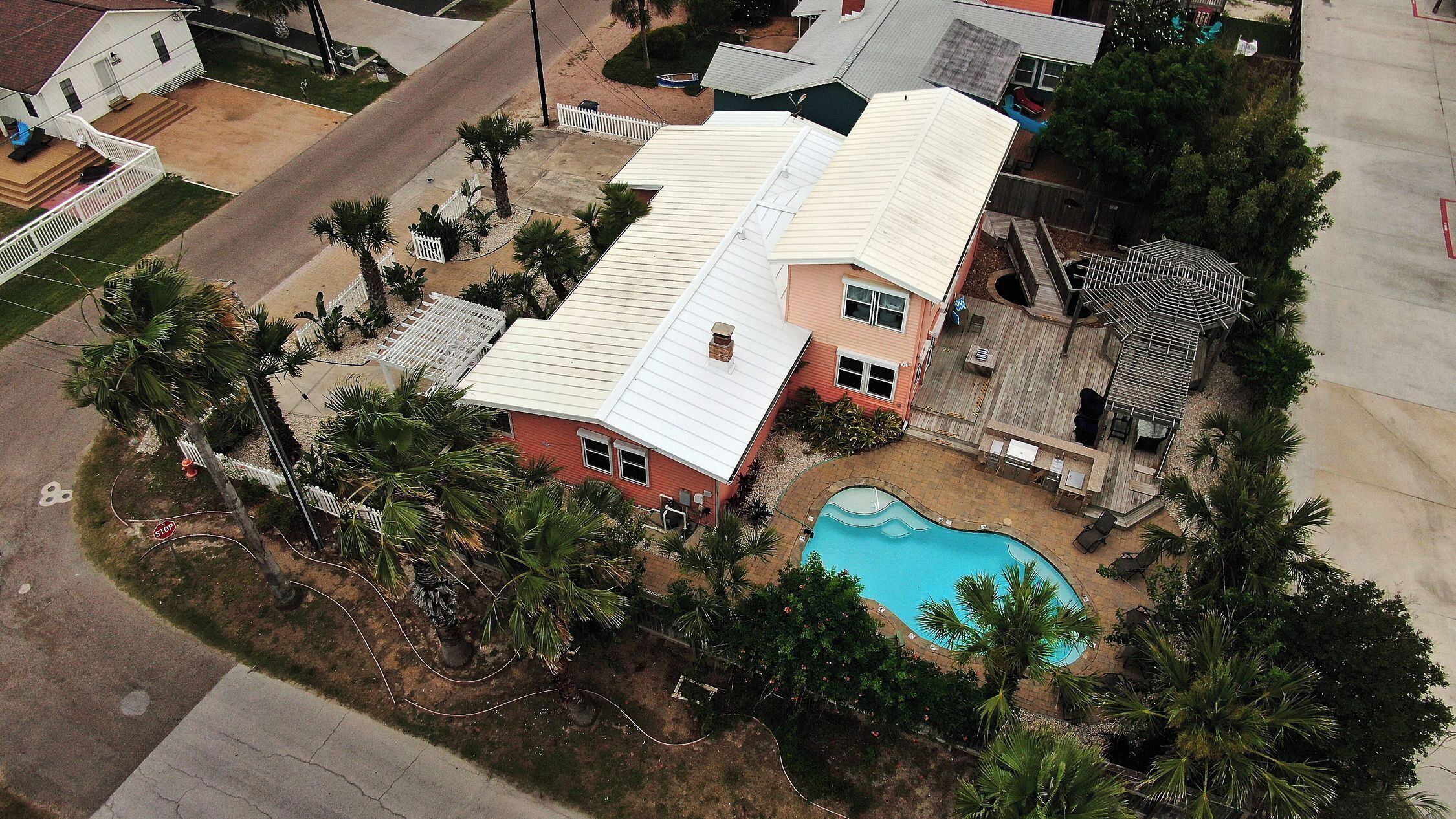 Una casa con piscina, rodeada de palmeras y un patio cercado.