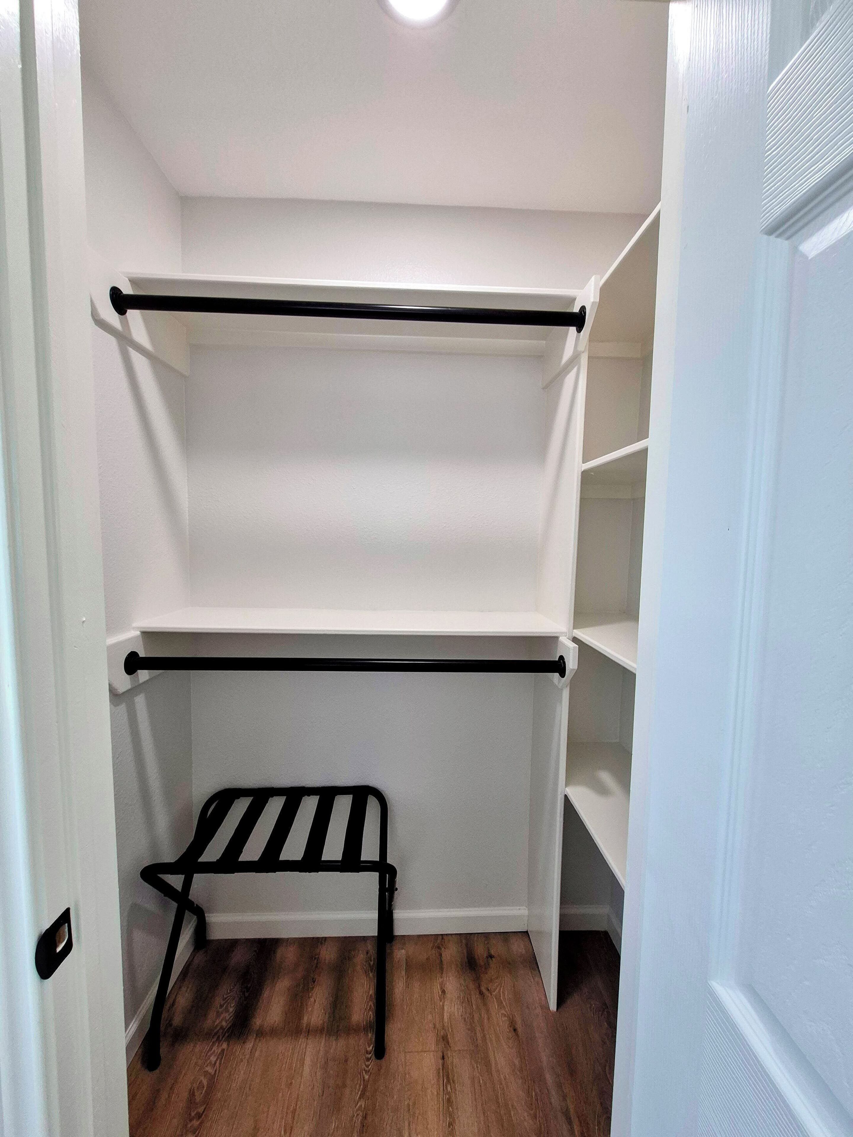 A walk-in closet with two black metal shelves and a black metal bench.