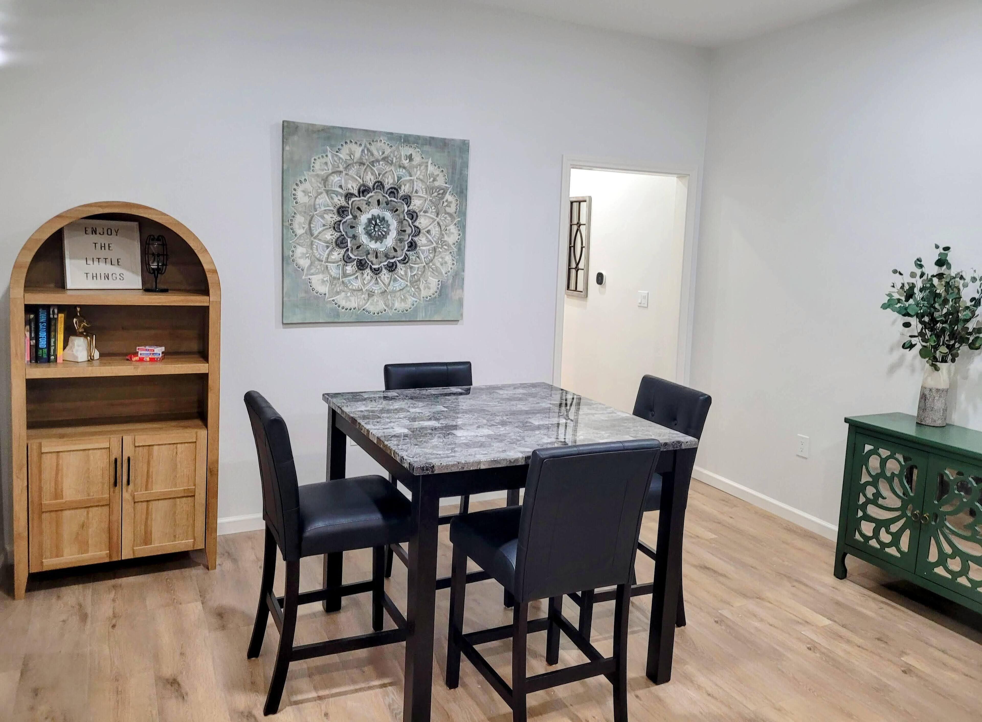 A dining area with a marble table, black chairs, a wooden bookshelf, and a green cabinet.