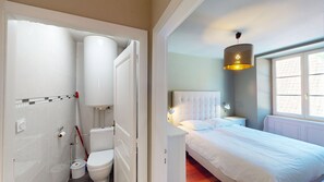 Ein Hotelzimmer mit Toilette, Bidet und Bidet-Sitz; ein Bett mit weißem Kopfteil und Nachttischlampe; ein Fenster mit Blick; und eine hängende Leuchte.