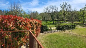 Ein Garten mit einer Holzterrasse, einer Steinmauer und verschiedenen Bäumen und Sträuchern.