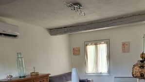 Ein Essbereich mit einem Tisch für vier Personen, einem Holzschrank, einer Couch und einem Fenster mit Vorhängen.