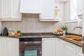 A modern kitchen with white cabinets, a Bosch oven, a sink, and a countertop with a fruit bowl and a coffee maker.