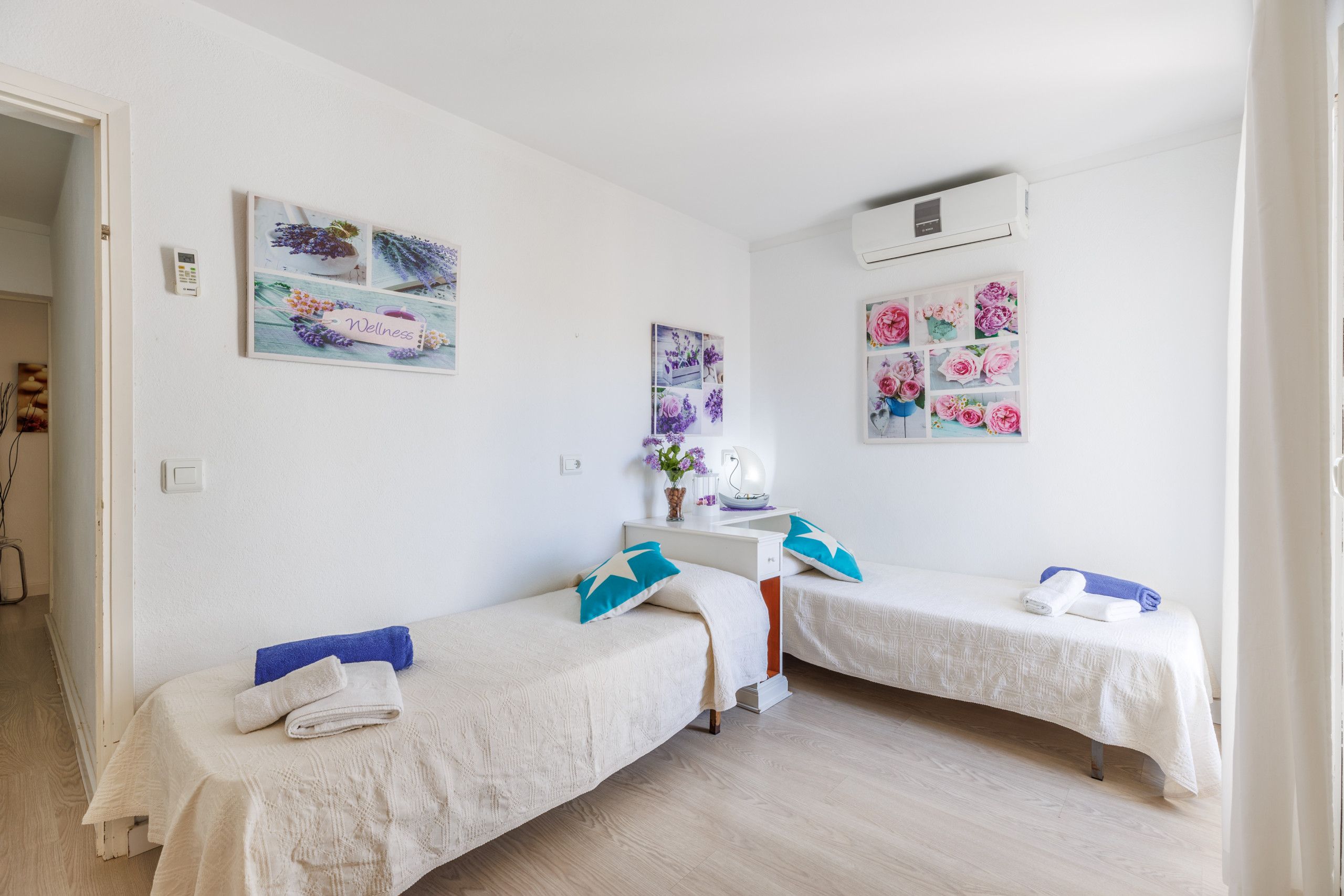 Una habitación limpia y bien iluminada con dos camas individuales, un escritorio con silla y decoración en la pared.