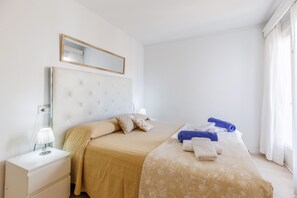 A hotel room with a large bed, a bedside table with a lamp, a mirror above the bed, and a window with curtains.