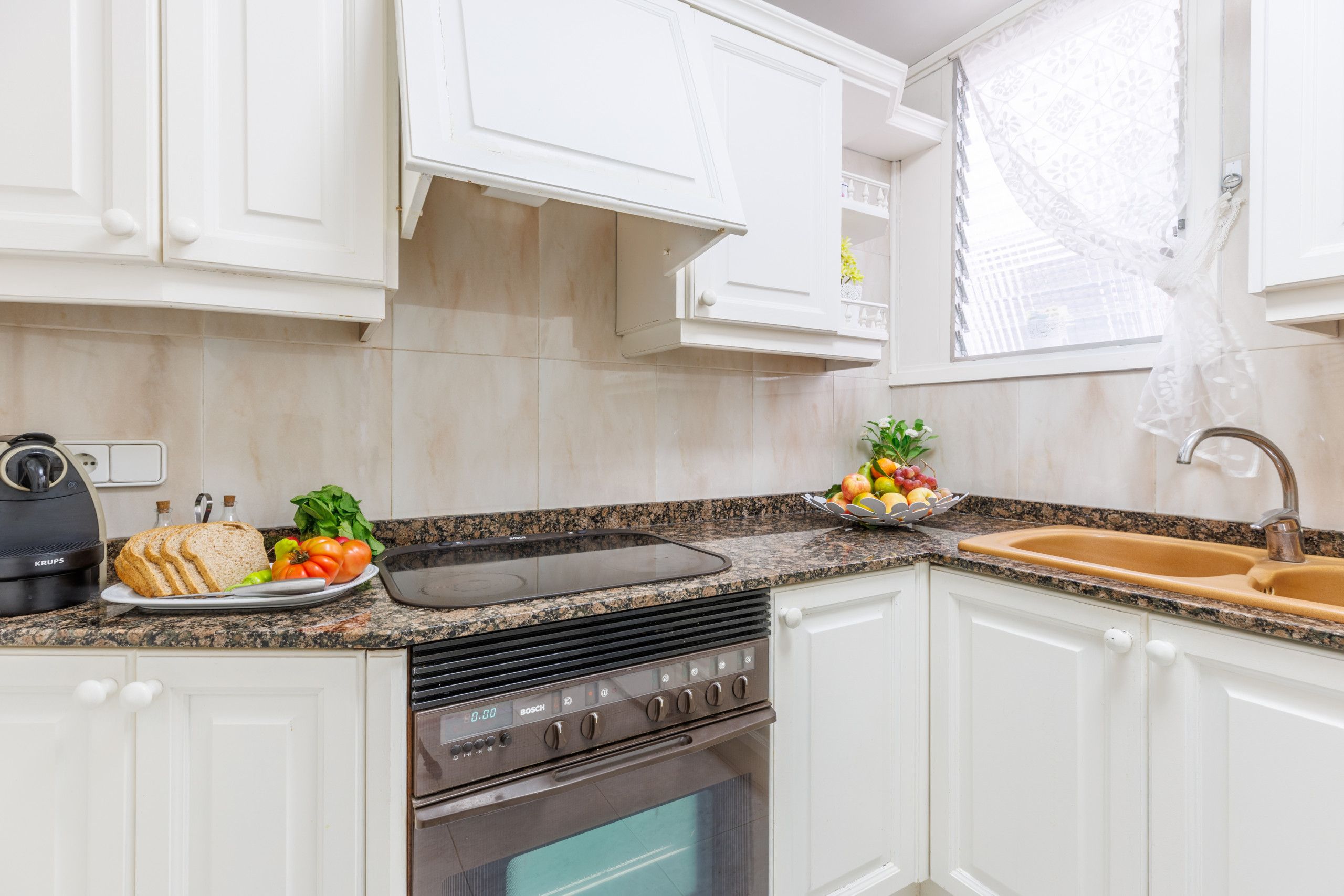 A modern kitchen with white cabinets, a Bosch oven, a granite countertop, and a sink.