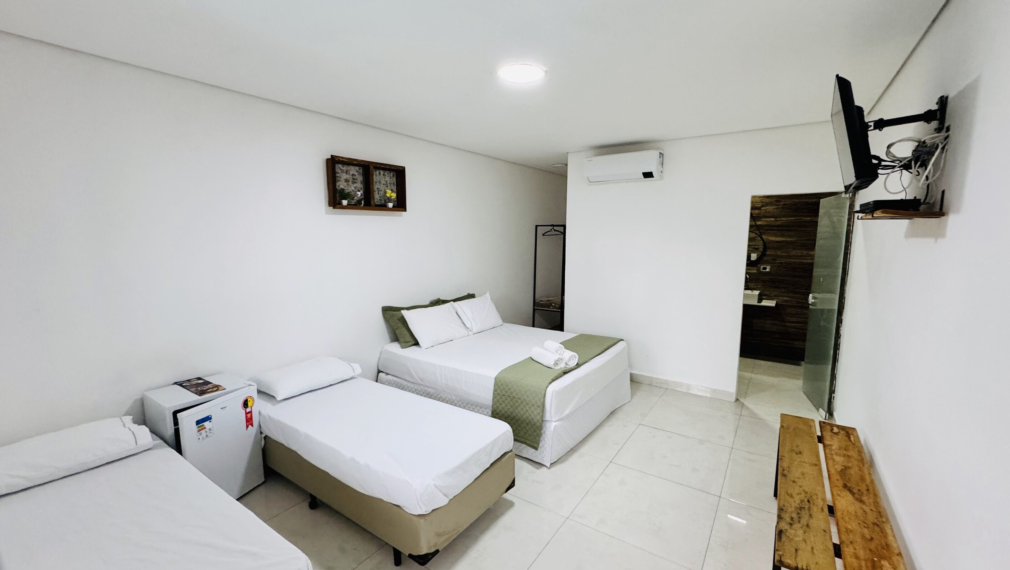 Une chambre d’hôtel avec deux lits simples, une petite table de chevet avec une lampe, un miroir et un téléviseur fixé au mur.