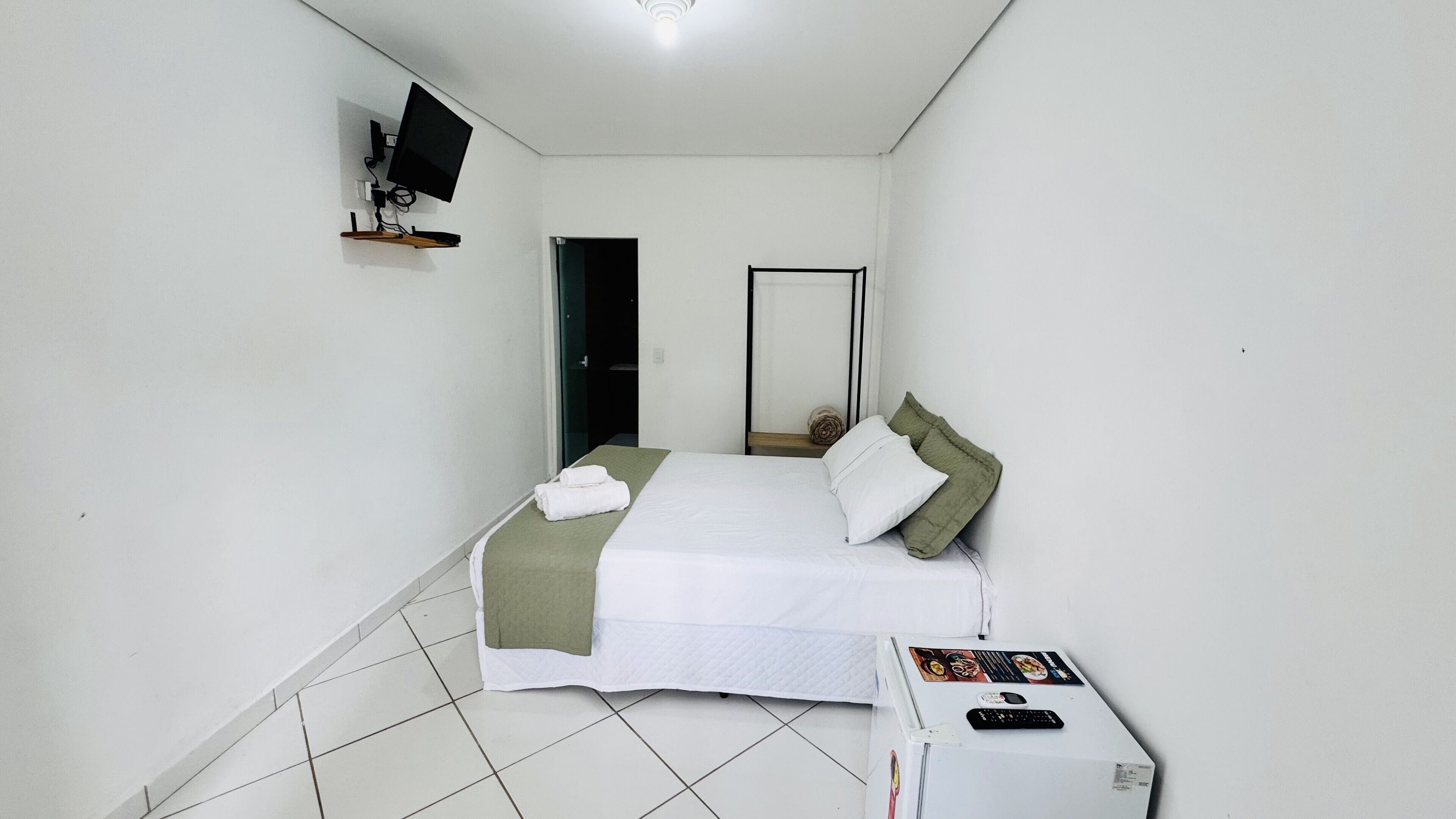 A bedroom with a bed, a TV mounted on the wall, and a small table with a remote control.