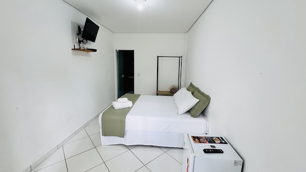Un dormitorio con una cama, un televisor montado en la pared y una mesita con un control remoto.