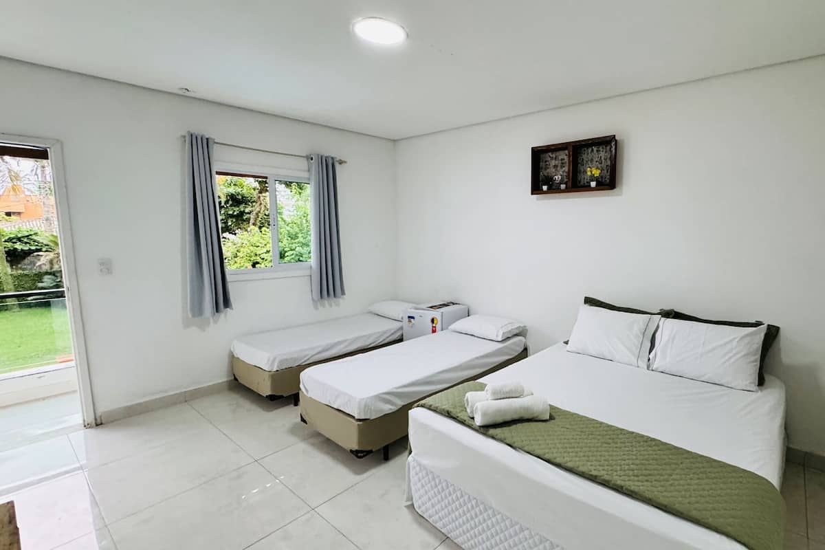 Une chambre d’hôtel avec deux lits simples, une grande fenêtre avec des rideaux, une petite table et un tableau au mur.